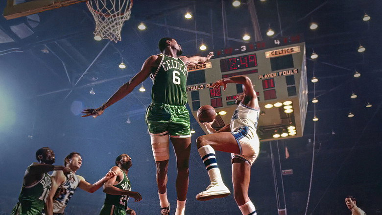A black-and-white photograph of Bill Russell mid-game, his arms outstretched, eyes locked on the ball, the court a blur of motion around him