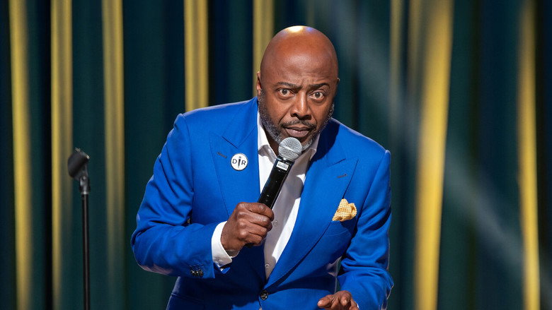 Donnell Rawlings on stage in a blue suit, mid-performance, with a microphone in hand