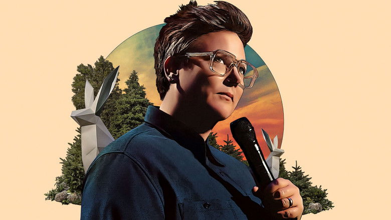 Hannah Gadsby on stage, mid-gesture, bathed in warm light, the Sydney Opera House’s iconic sails visible in the background