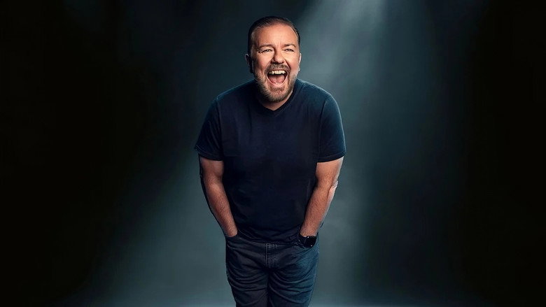 Ricky Gervais on stage in a black suit, mid-gesture, with a spotlight casting long shadows