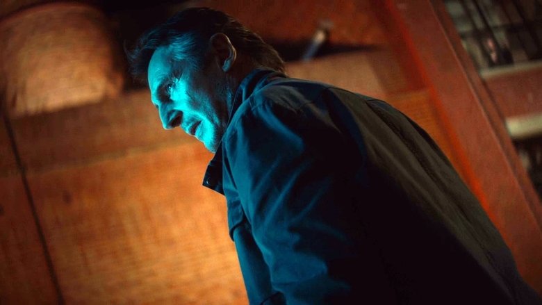 Liam Neeson standing in a dimly lit, blue-tinted office, looking at a computer screen with a weary expression.