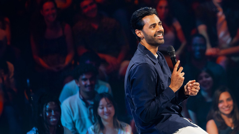 Minhaj on stage, bathed in a single spotlight, his expression caught between a grin and a grimace