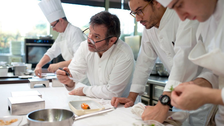 A chef's hands delicately plating a dish, the colors of the food vibrant against the dark background