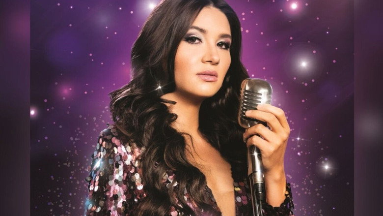 A dimly lit room where a young woman sings into a microphone, her face half in shadow, her posture tense with effort.