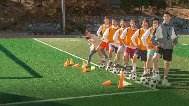 A wide shot of the makeshift soccer team huddled together on a rain-soaked field, their faces a mix of exhaustion and determination.