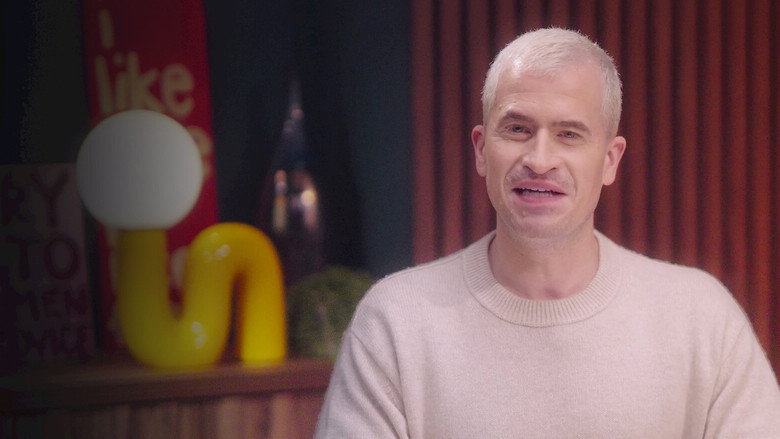 Evan Ross Katz leans forward in a dimly lit studio, his expression earnest as he listens to a guest just out of frame.