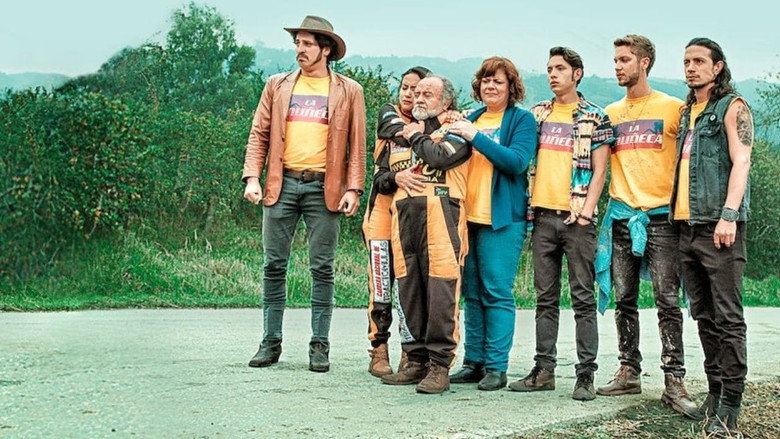 A dusty Colombian highway stretches into the distance, flanked by cargo trucks with vibrant, hand-painted designs. The sky is a hazy gold, the kind of light that makes even a truck stop look like a postcard.
