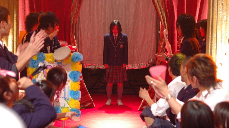 Two boys in school uniforms stand over a girl sitting on the ground, their expressions a mix of determination and mischief