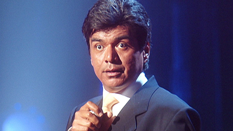 George Lopez on stage, mid-laugh, gesturing to the audience