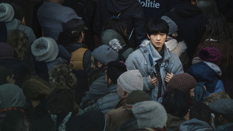 Loh Kiwan standing alone in a dimly lit Brussels train station, his breath visible in the cold air.