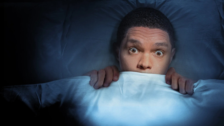 Trevor Noah on stage, mid-gesture, bathed in warm light