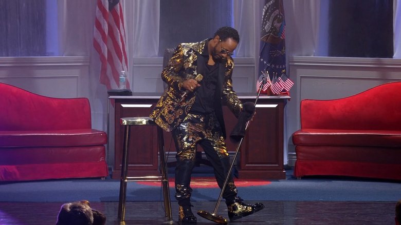 Katt Williams mid-performance, arms outstretched, bathed in stage light