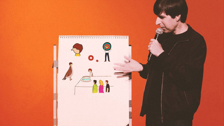 Demetri Martin standing on stage with a whiteboard, marker in hand, mid-explanation.