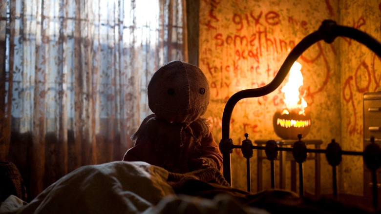 A group of teenagers in Halloween costumes stand in a dimly lit street, their faces half-lit by jack-o'-lanterns, as something unseen lurks in the shadows behind them.