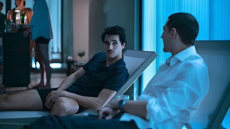 Amir and his father sit across from each other at a dimly lit table, the tension between them palpable as the glow of a laptop screen casts shadows on their faces.