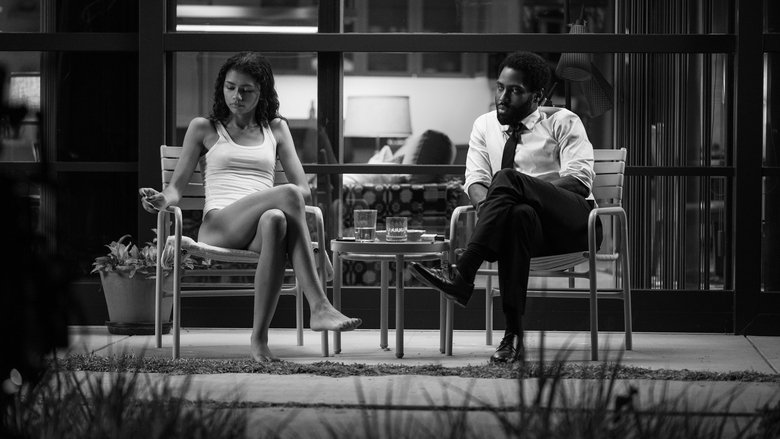 A black-and-white shot of Malcolm and Marie standing in a stark, modern kitchen, their faces half-lit by the overhead light, tension hanging between them like smoke.
