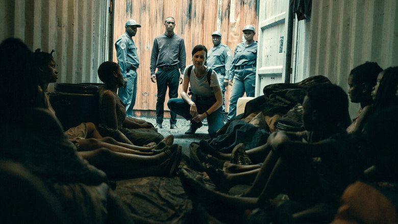 A dimly lit room where Jodie and Ntombizonke stand on opposite sides of a table, their reflections warped in the polished surface.