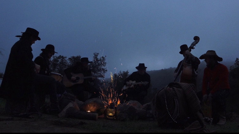 A group of musicians sit in a desert landscape, their instruments resting beside them as the golden hour light casts long shadows.