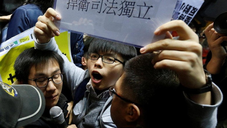 Joshua Wong, 14, addresses his classmates from a folding chair, his hands gripping the metal frame tightly.