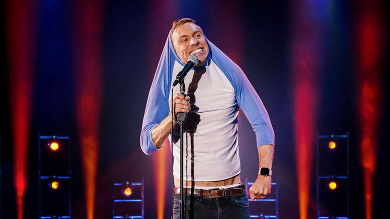 Russell Howard on stage, mid-gesture, bathed in warm light