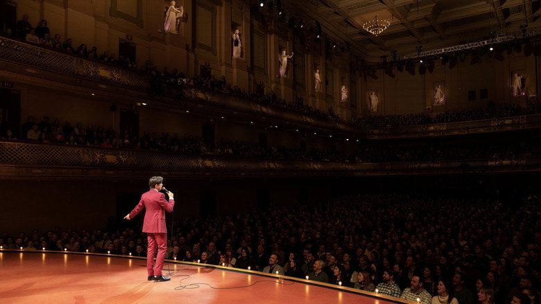 Mulaney in a bright red suit under stage lights, mid-gesture