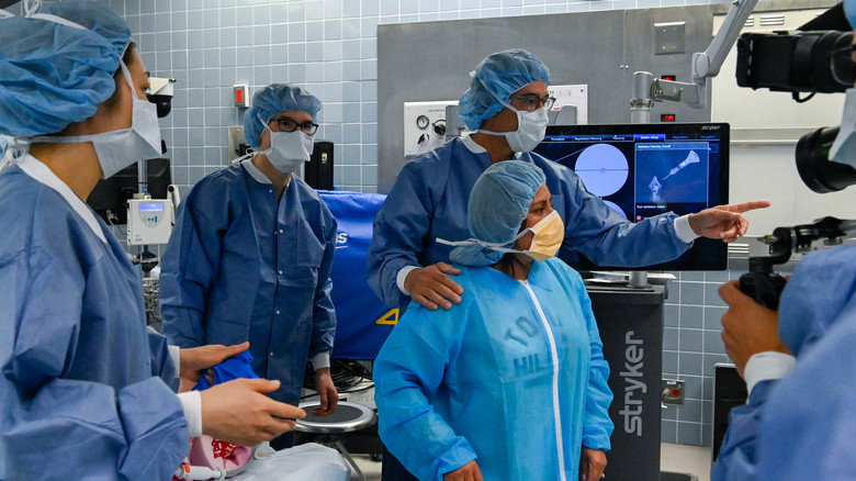 A surgeon's gloved hands adjust a surgical tool during an operation, the sterile blue of the operating room filling the frame.