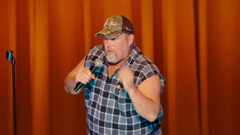 Larry the Cable Guy on stage, arms outstretched, in front of a red curtain