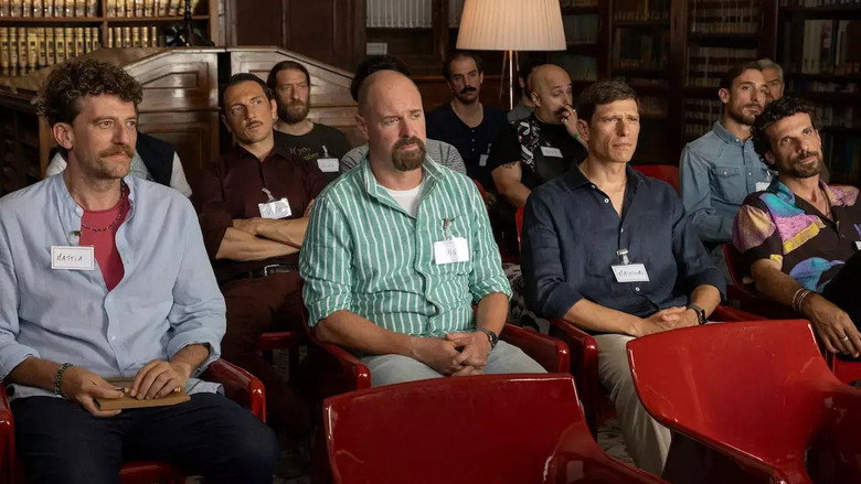 Four middle-aged men sitting in a circle, looking uncomfortable, with a facilitator standing over them