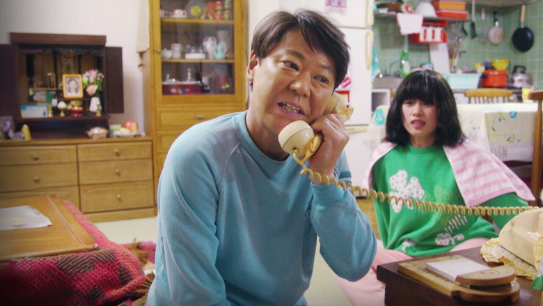 Ichiro Ogawa, cigarette dangling from his lips, stares in horror at a 2024 classroom where students hold protest signs about "emotional safety."