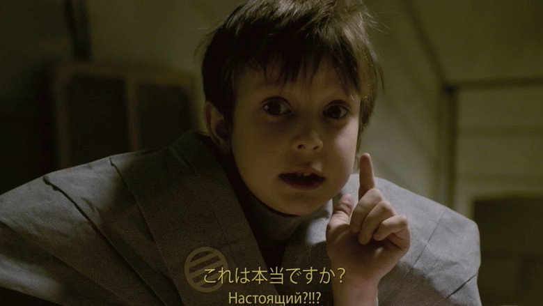 A child’s hand reaches for a bottle of vodka on a cluttered kitchen table, the light filtering through a grimy window.