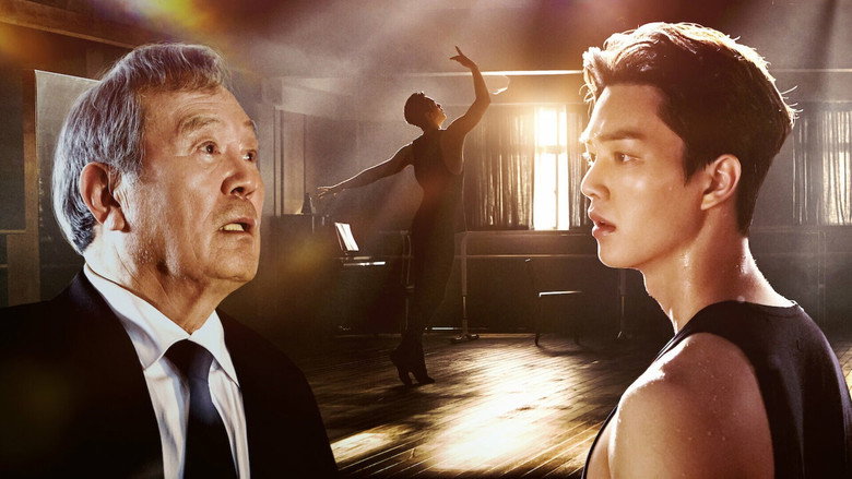 A 70-year-old man watches a ballet class from the back of the studio, his reflection faint in the mirror, his hands curled into loose fists at his sides.