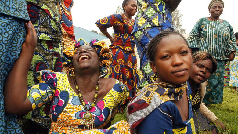 A group of women in colorful dresses stand together, their faces lit with cautious smiles, as they participate in a workshop at the City of Joy.
