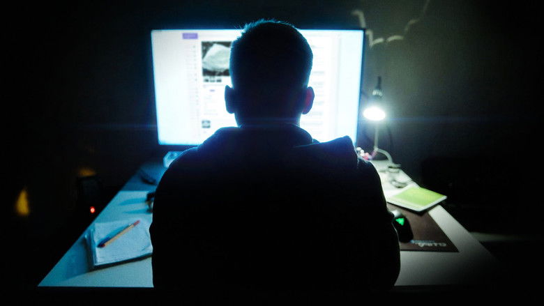 A dimly lit bedroom, glow of a laptop screen illuminating a young man's face