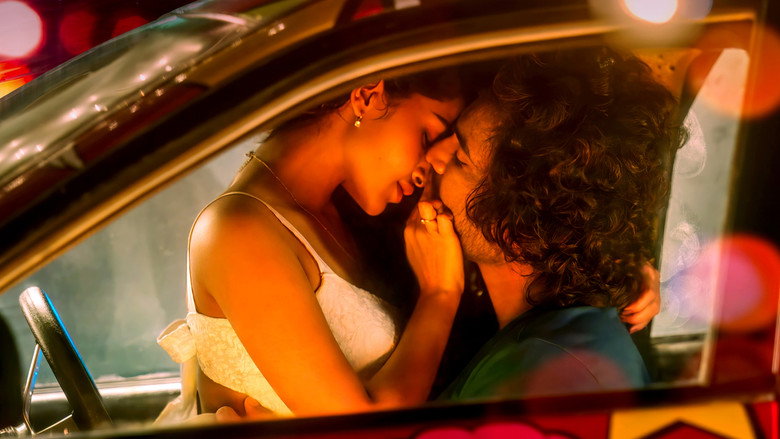 Tillu and Lilly share a tense moment in a dimly lit room, the glow of a neon sign casting long shadows across their faces.