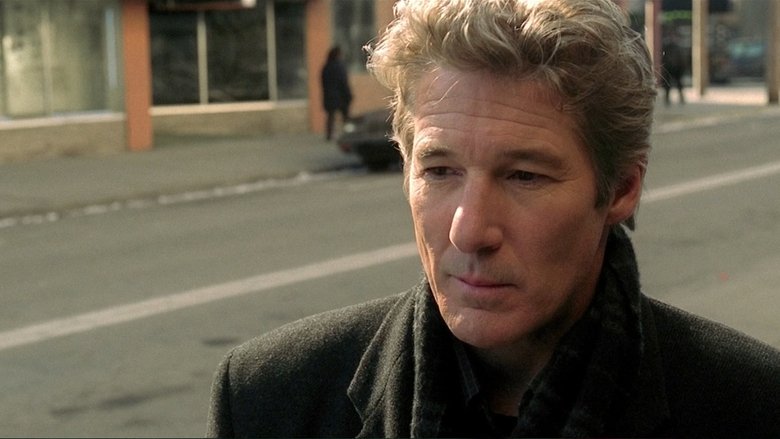 A shadowy figure looms over Richard Gere in a dimly lit room, the camera tilted to heighten the unease.