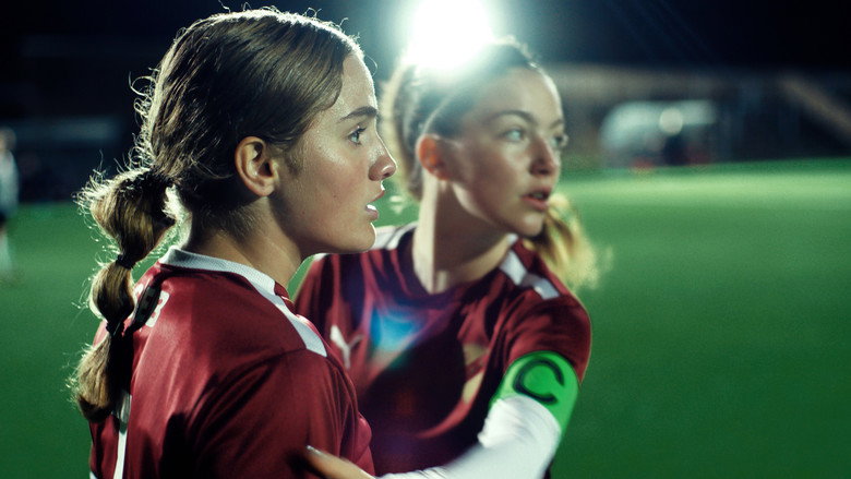 Two teenage girls in football kits sit side by side on a bench, their faces lit by the low sun of a Swedish summer evening.