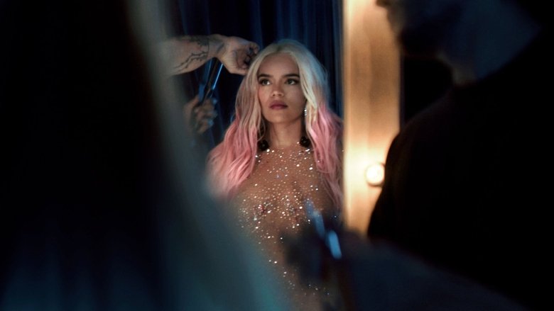 Karol G on stage, bathed in pink light, her arms raised as confetti falls around her
