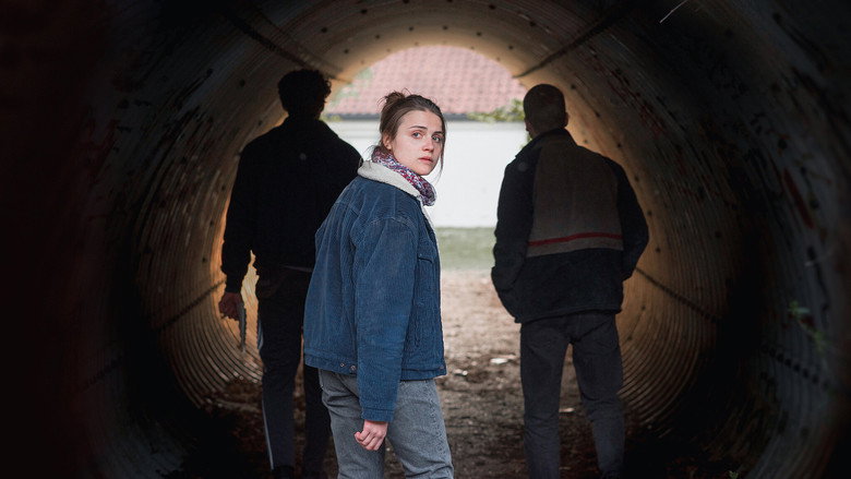 A dimly lit room where Luisa and her friends huddle around a laptop, the glow of the screen casting sharp shadows on their faces.