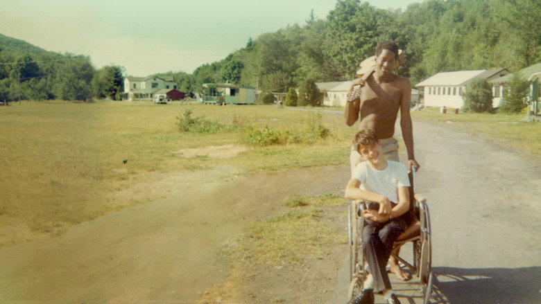 Teenagers at Camp Jened in the 1970s, laughing and talking in a grassy field