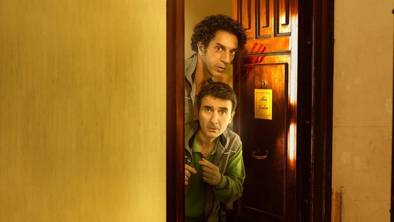 Two men in polo shirts stand in a cluttered room, one gesturing wildly while the other looks on with mild alarm